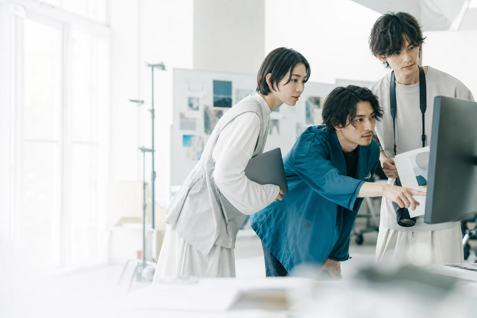 企画資料とデジタル画面を囲み、領域を横断して意見を交わすチーム